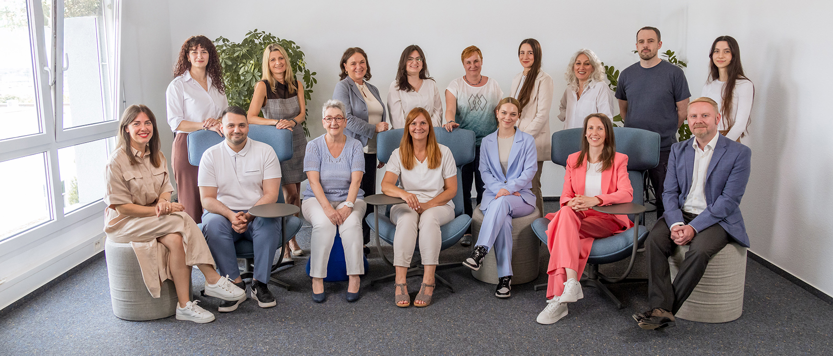 Gruppenfoto eines großen Teams in einem hellen Büroraum – die Mitarbeitenden sitzen und stehen in entspannter, professioneller Atmosphäre.